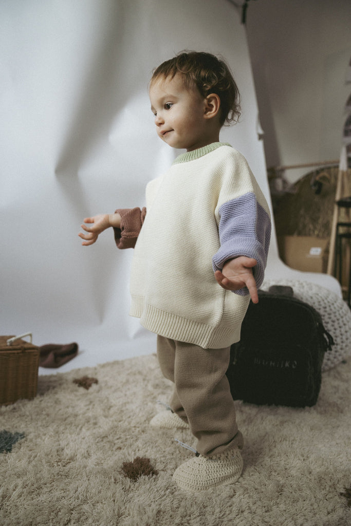 Fröhliches Kind mit einem cremefarbenen Pullover mit bunten Akzenten am Kragen und den Ärmeln