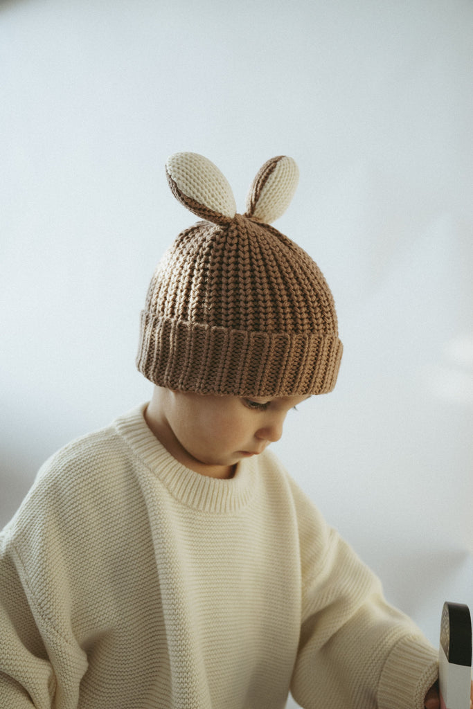 Süßes Kind mit goldiger Wollmütze mit Hasenohren und einem cremefarbenen Pullover aus Baumwolle 