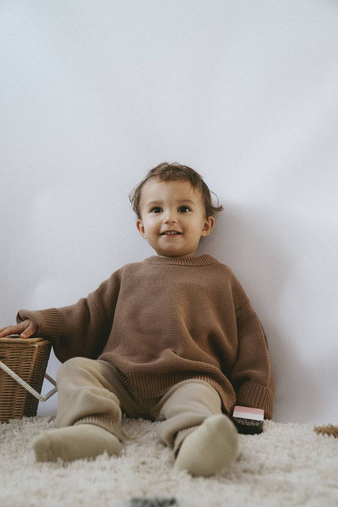 Grinsendes Kind mit einem braunen Pullover ein feiner Bio-Baumwolle mit einer Hose aus Strick.