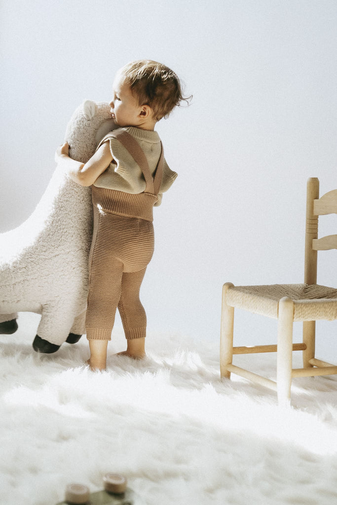 Kind umarmt ein Lama und hat eine Latzhose aus Baumwolle an 