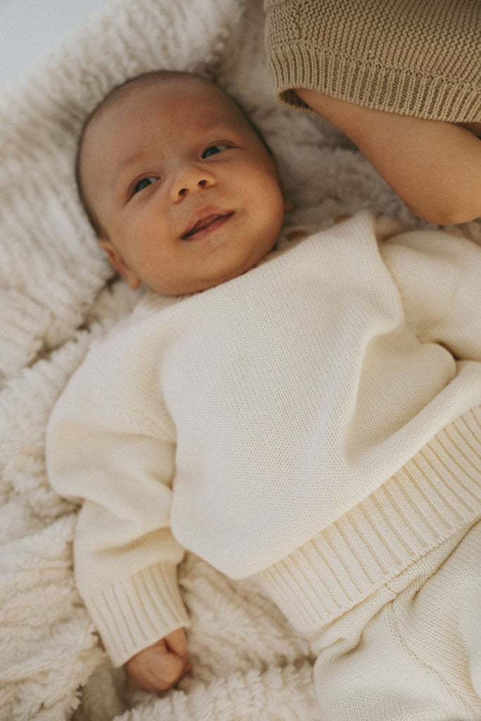 Süßes Baby trägt einen Strickpullover aus feiner Baumwolle in Creme