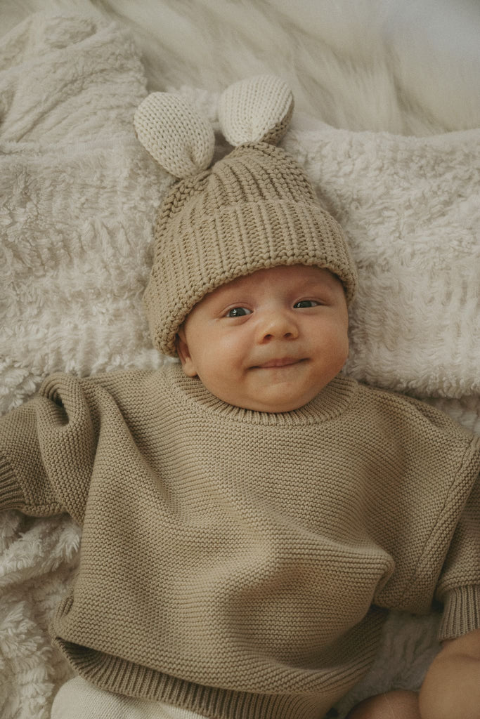 Süßes Baby mit goldiger Wollmütze mit Hasenohren und einem beigefarbenen Pullover aus Baumwolle