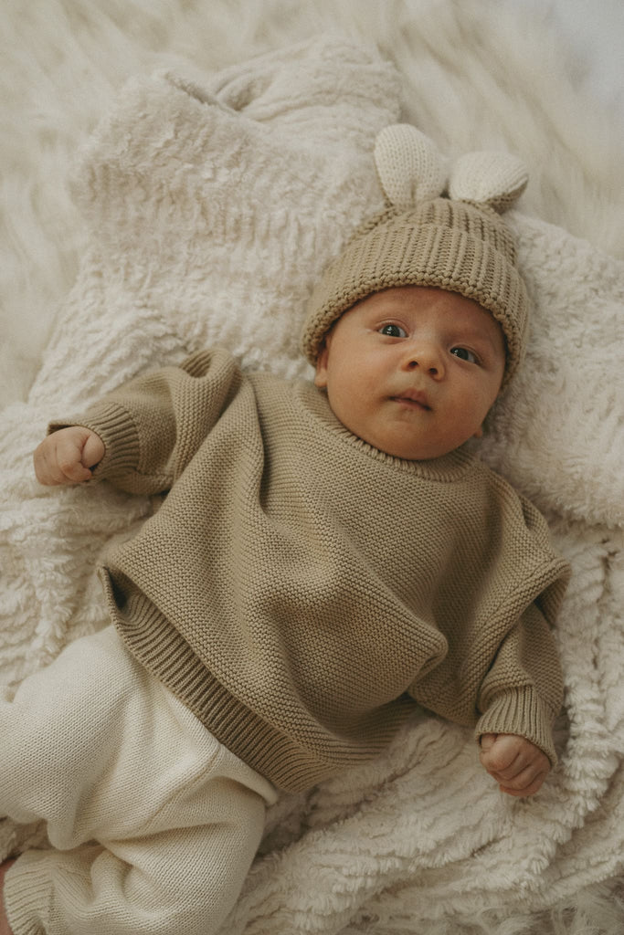 Goldiges Baby trägt eine Mütze mit Hasenohren und einem Pullover aus Bio-Baumwolle