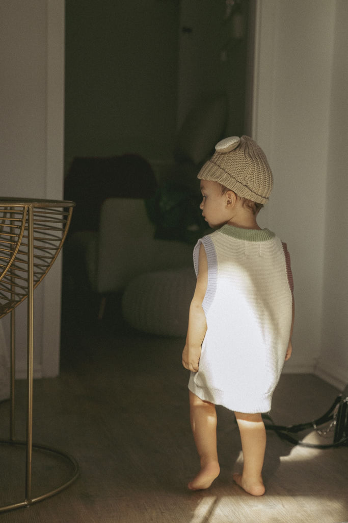 Kind mit süßer Hasenohren Mütze in Beige trägt einen cremefarbenen Pullunder mit einem bunten Kragen. 
