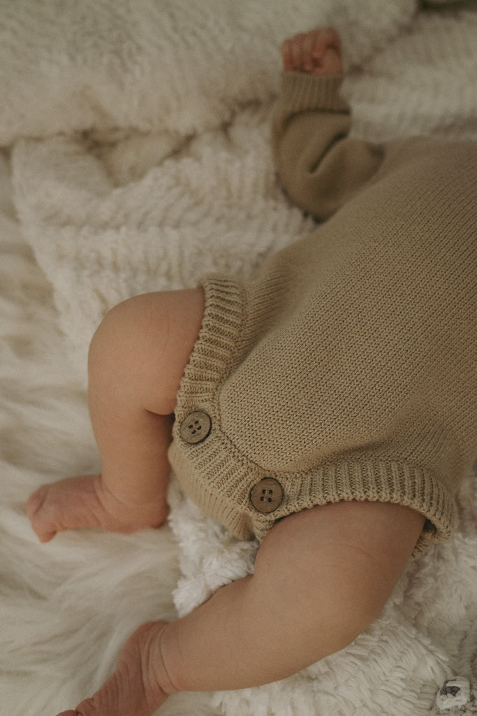 Goldige Füße eines Babys, welches einen beigen Body aus feiner Bio-Baumwolle trägt.