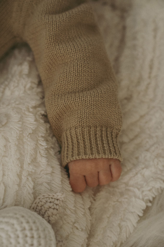 Goldiges Händchen eines Babys, welches einen beigen Body aus feiner Bio-Baumwolle trägt.